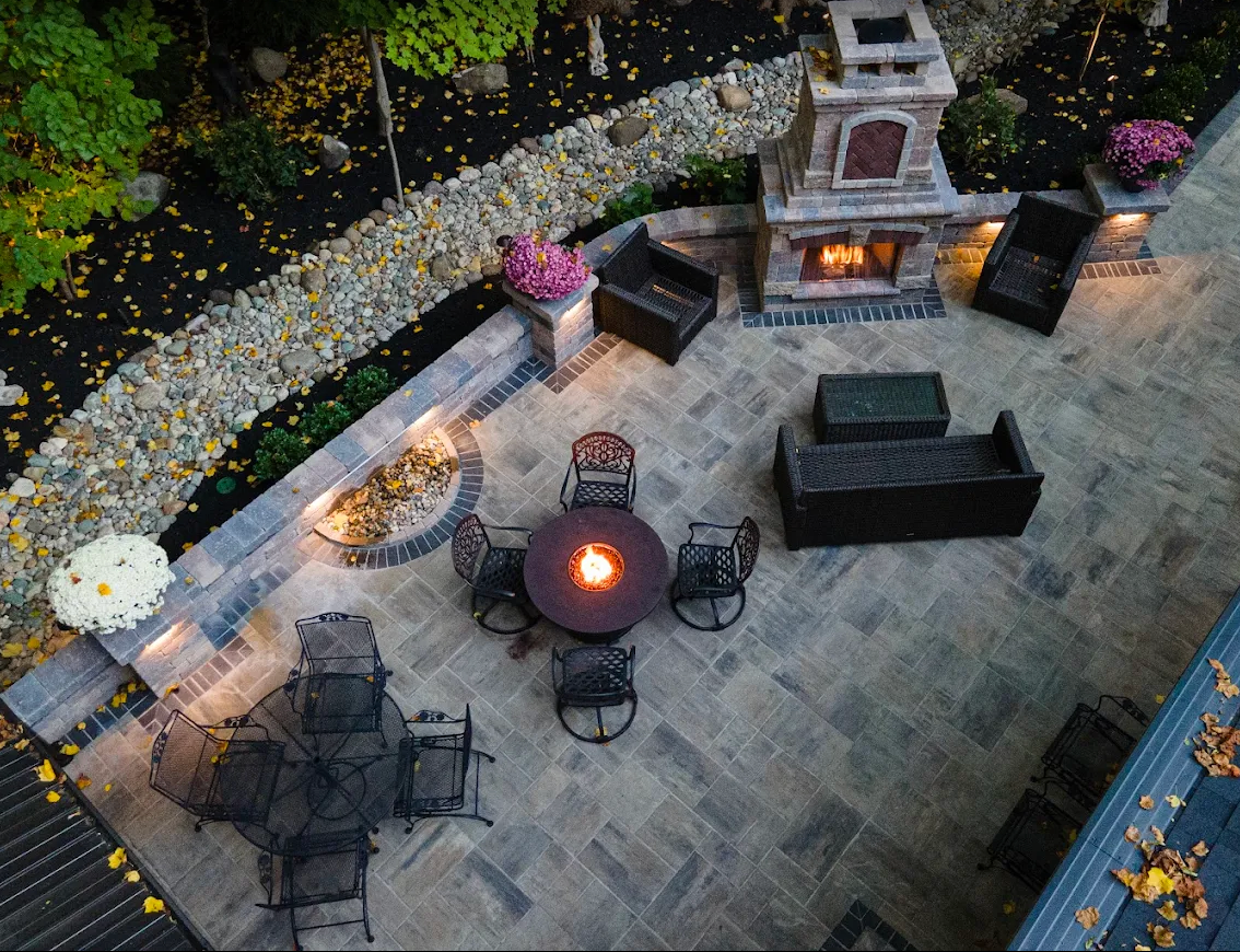 Finished paver patio with fire table and stone fireplace at dusk